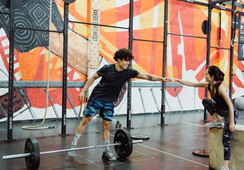Cheerful gym interaction between a man and woman sharing a fist bump in a vibrant fitness environment.